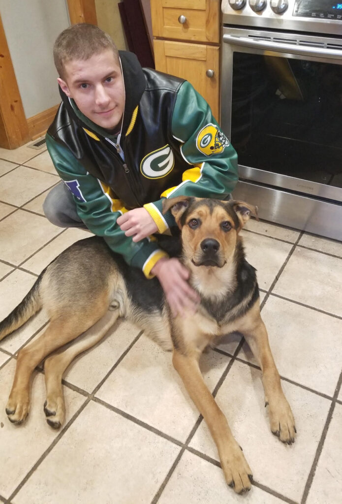 Sam sitting on a kitchen floor beside his dog, sharing a quiet and loving moment that reflects companionship, warmth, and connection